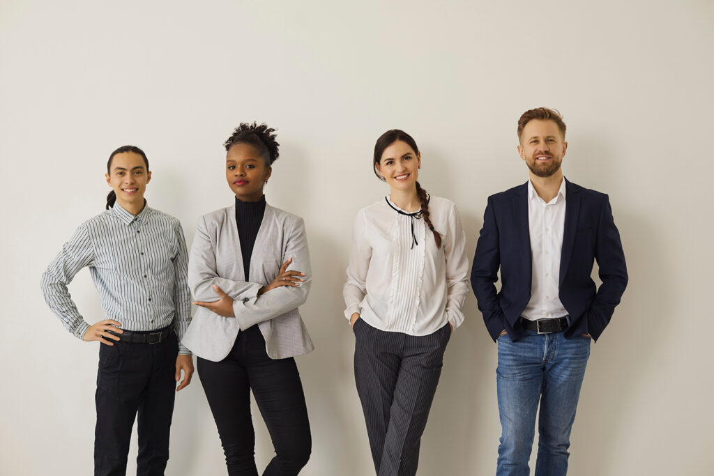 Group portrait of diverse office workers or job candidates. Team of happy confident multiracial business people in formal and smart casual wear standing near studio wall, smiling and looking at camera